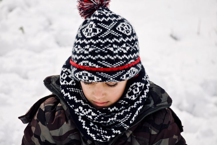 Enfant qui porte un bonnet et une écharpe assortis ainsi qu'une doudoune